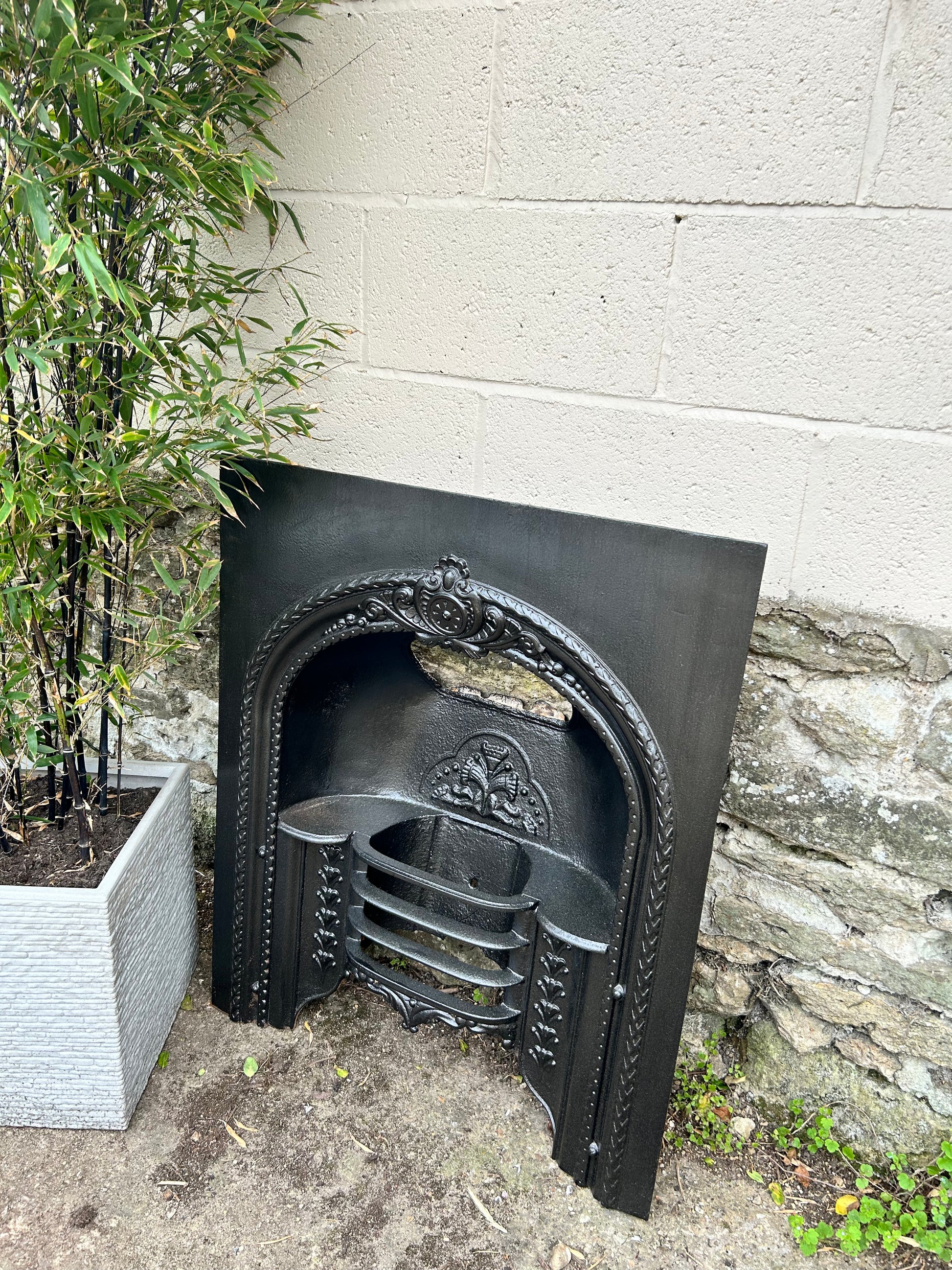 Cast iron fireplace insert against a stone wall with plants in the background